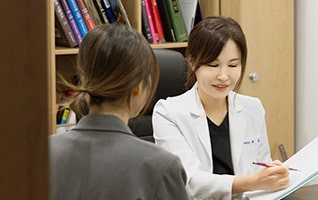 책장 앞 진료실에서 환자와 상담하며 기록하는 최경희 대표원장